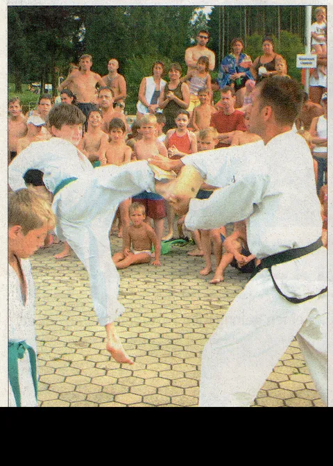 Foto Traunreuter Anzeiger vom 20. Juli 2004: Ein junger Taekwon-Do-Schüler mit grünem Gürtel tritt ein von Thomas Könnecke gehaltenes Brett in Kopfhöhe, dahinter Kinder und Eltern in Badekleidung im Freibad Traunreut