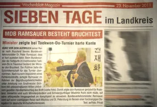 Zeitungsausschnitt „MdB Ramsauer besteht Bruchtest“ aus dem Wochenblatt-Magazin vom 23. November 2011: Bundesverkehrsminister Dr. Peter Ramsauer im Anzug schlägt mit der Handkante durch ein gehaltenes Holzbrett
