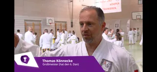 Screenshot TV Ingolstadt vom 26. Mai 2026: Thomas Könnecke im Interview in der Anton-Wolf-Halle Geisenfeld, Bauchbinde „Thomas Könnecke – Großmeister (hat den 6. Dan)", im Hintergrund trainierende Kinder und Erwachsene