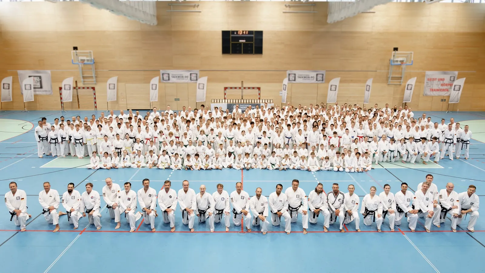 Gruppenfoto zum 25-jährigen Jubiläum der Taekwon-Do Schulen Könnecke im Sportzentrum Nord Salzburg: vorne kniend 27 Großmeister mit Schwarzgurt, dahinter hunderte Teilnehmer aller Gürtelfarben
