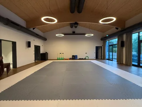 Neuer Trainingsraum der Taekwon-Do-Gruppe Bernau am Chiemsee mit grau-weißer Mattenfläche unter einer geschwungenen Holzgewölbedecke mit Ringleuchten