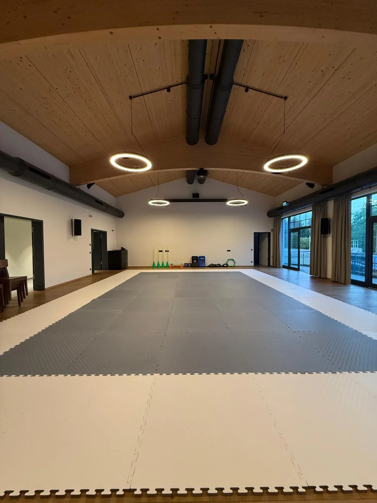 Neuer Trainingsraum der Taekwon-Do-Gruppe Bernau am Chiemsee mit grau-weißer Mattenfläche unter einer geschwungenen Holzgewölbedecke mit Ringleuchten
