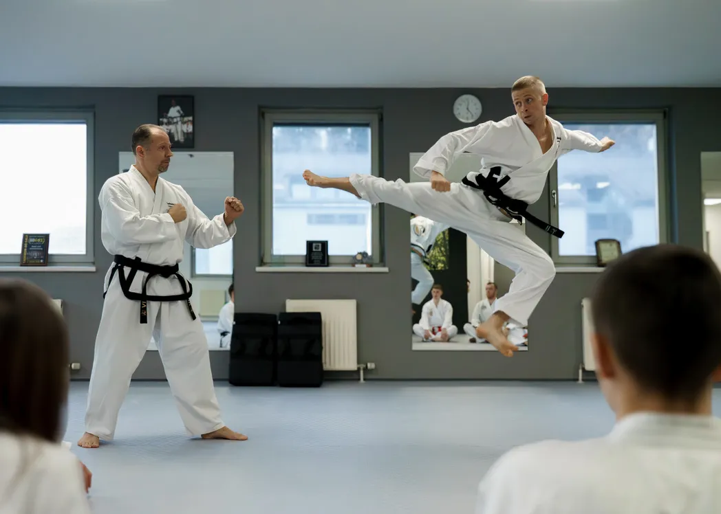 Erwachsenentraining bei Taekwon-Do Übersee – Trainer zeigt einen Flugkick, zwei Kinder beobachten das Training