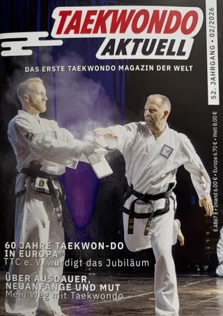 Titel der Ausgabe 02/2026 von Taekwondo Aktuell: Großmeister Thomas Könnecke zerbricht beim Fingerspitzen-Bruchtest ein gehaltenes Holzbrett im Münchner Circus Krone Bau.