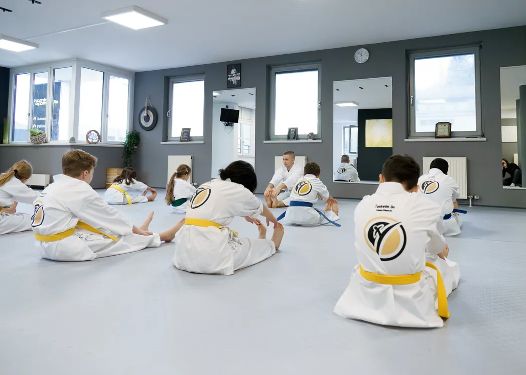 Taekwon-Do-Training bei den Taekwon-Do Schulen Könnecke – Kinder dehnen sich im Sitzkreis, ein Trainer leitet die Übung an