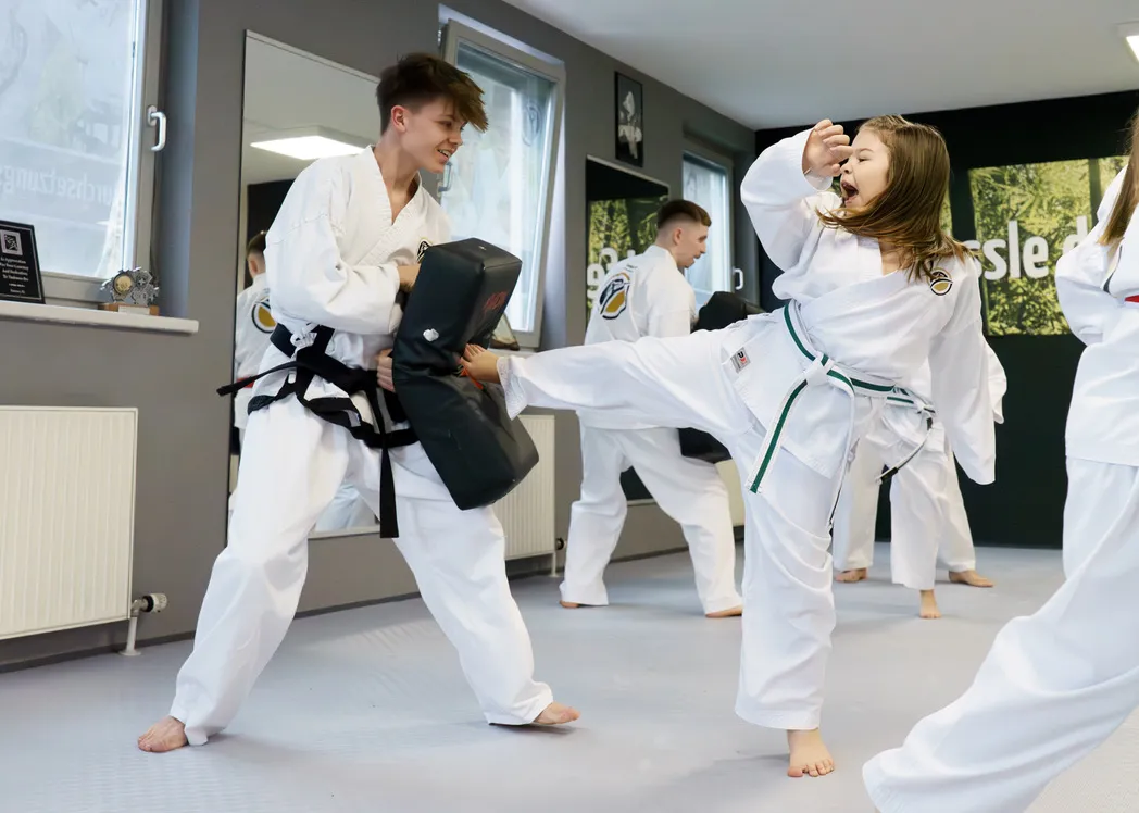 Taekwon-Do-Training bei den Taekwon-Do Schulen Könnecke – Kind kickt konzentriert gegen ein Pratzenpolster, der Trainer hält dagegen